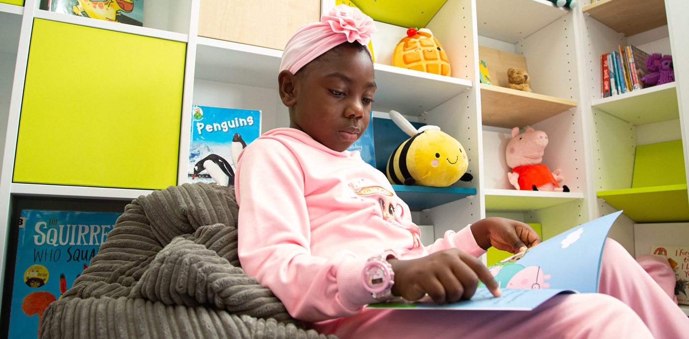 An image of a young girl sat on a bean bag reading a book in the library