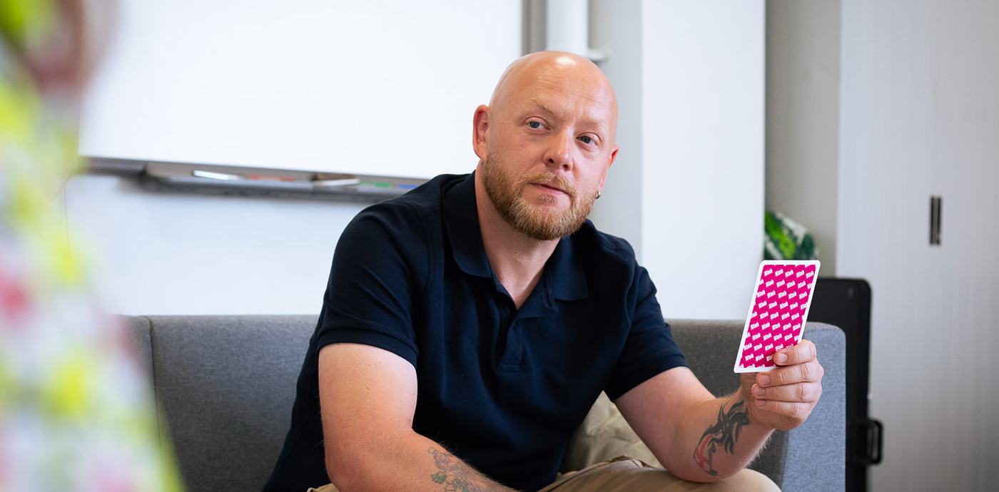 A middle aged man sat on a sofa reflecting on the content of a question card he is holding
