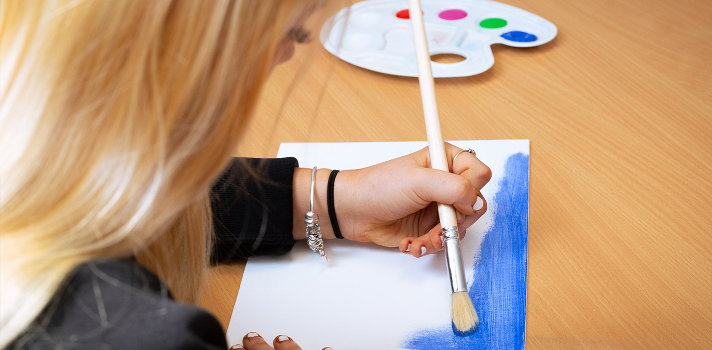An image of a teenage girl at a desk with palette painting on a piece of paper