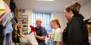 A smiling woman shows a young person a school uniform sweater